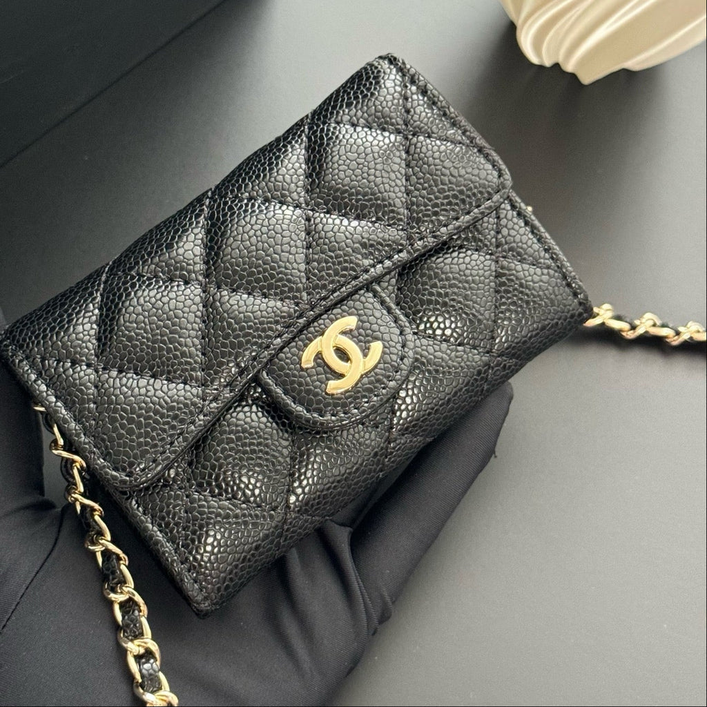 Black quilted handbag with gold chain and logo on a gray surface