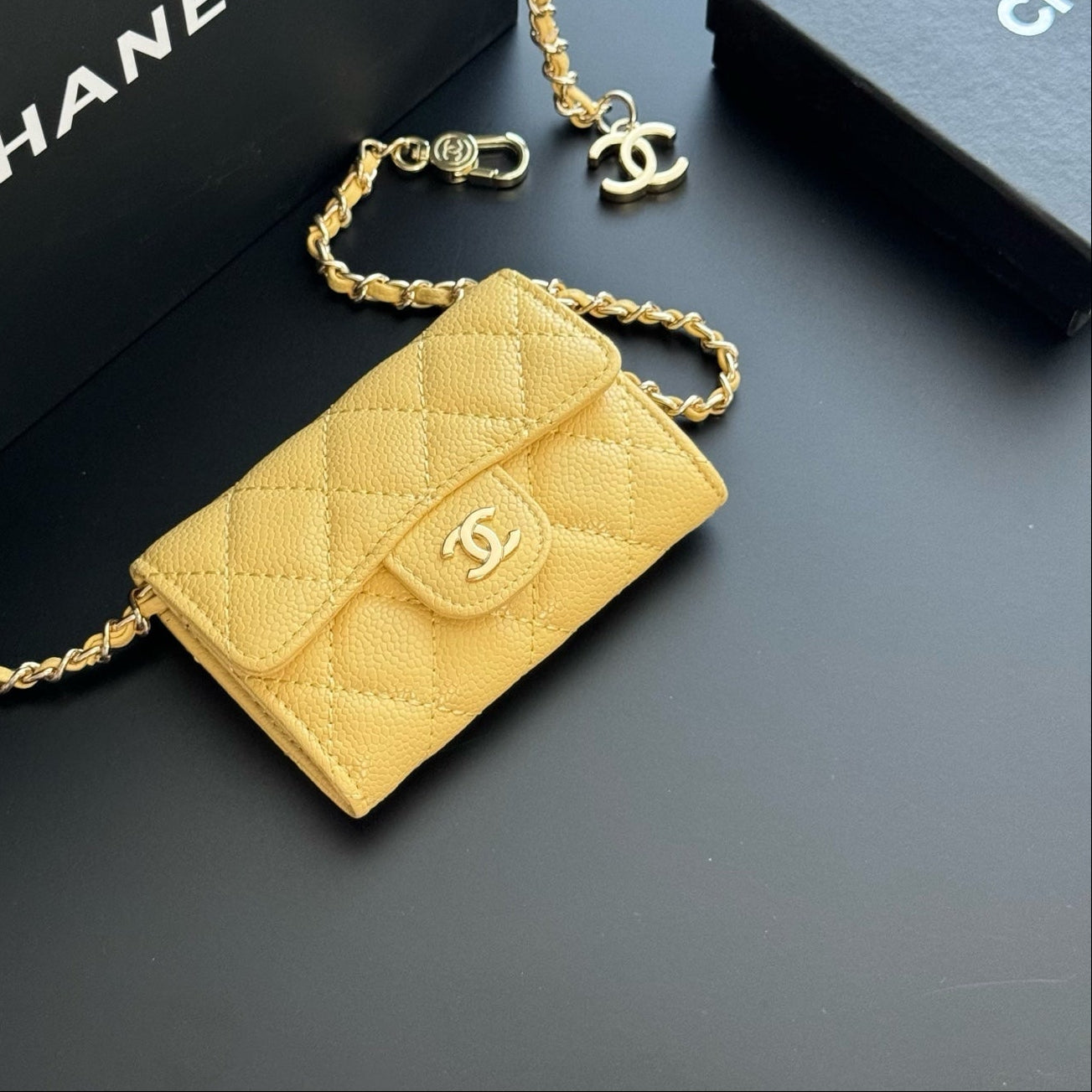 Yellow quilted handbag with gold chain on a dark background, featuring Chanel branding.