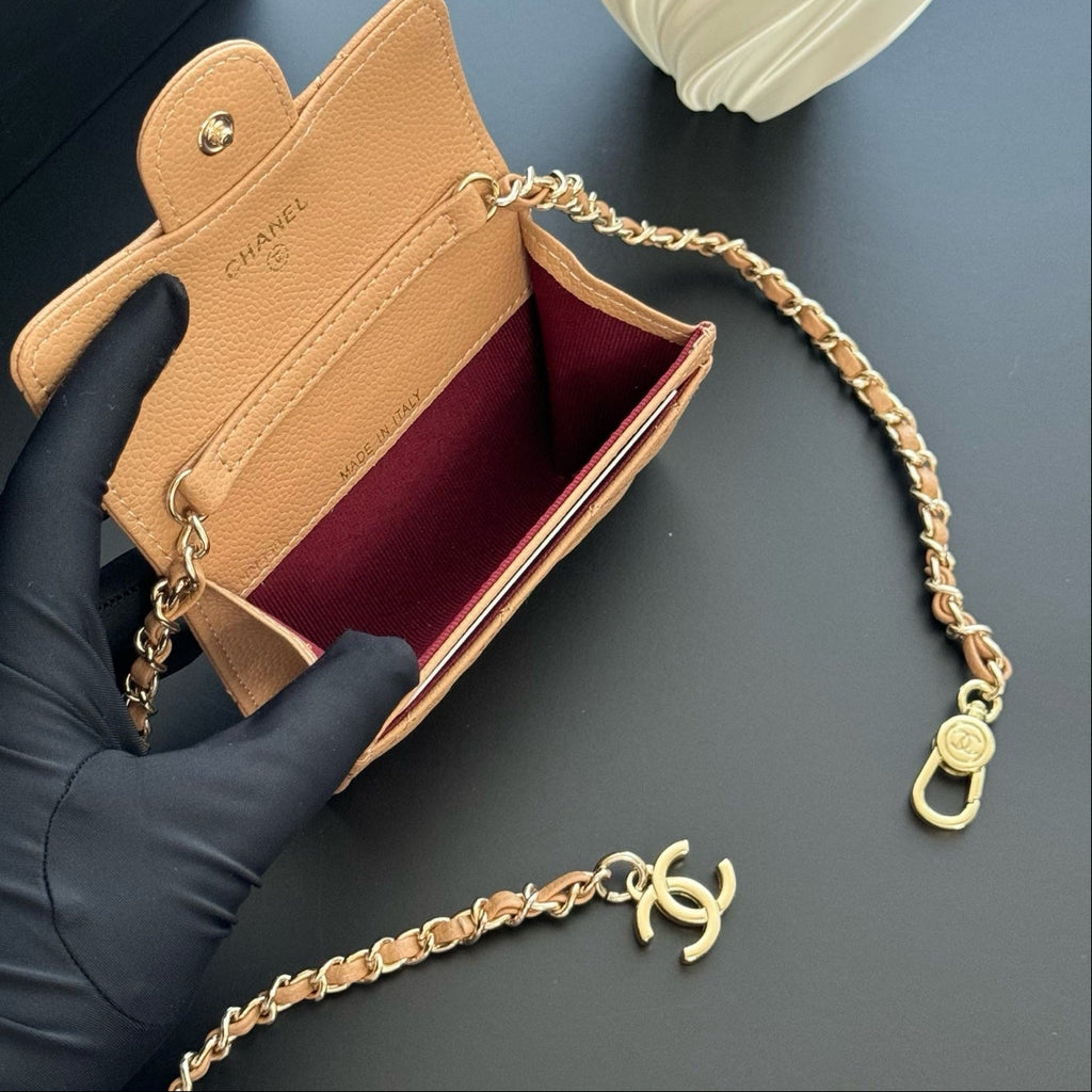 Chanel wallet with gold chain held by a gloved hand on a dark surface