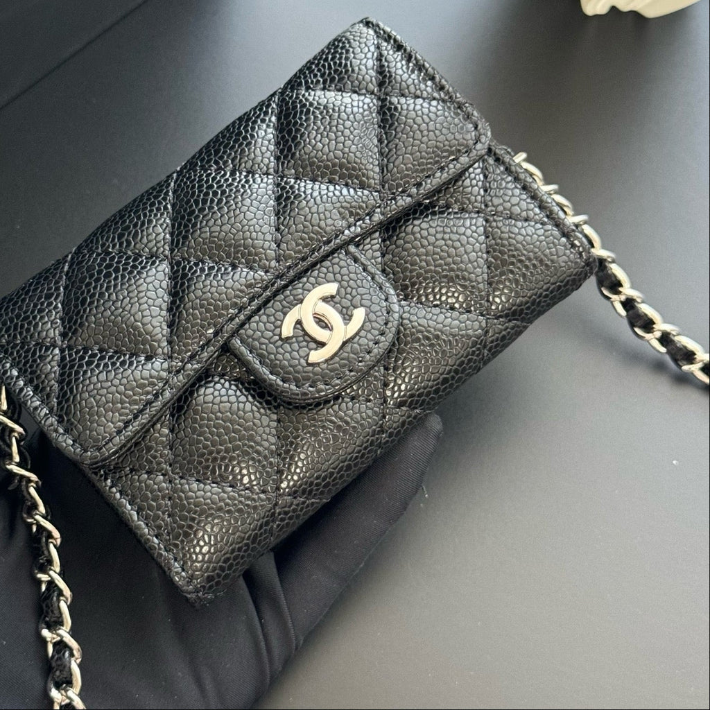 Black quilted handbag with gold chain on a dark surface