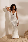 Woman wearing a white crochet dress standing against a neutral wall.