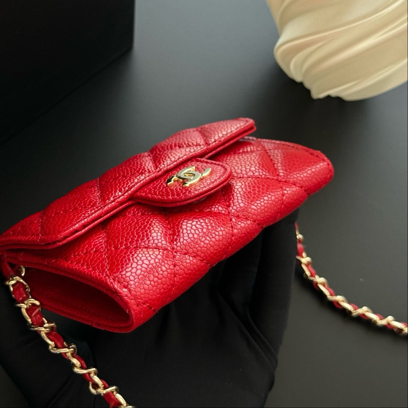 Red handbag with gold chain on a dark surface