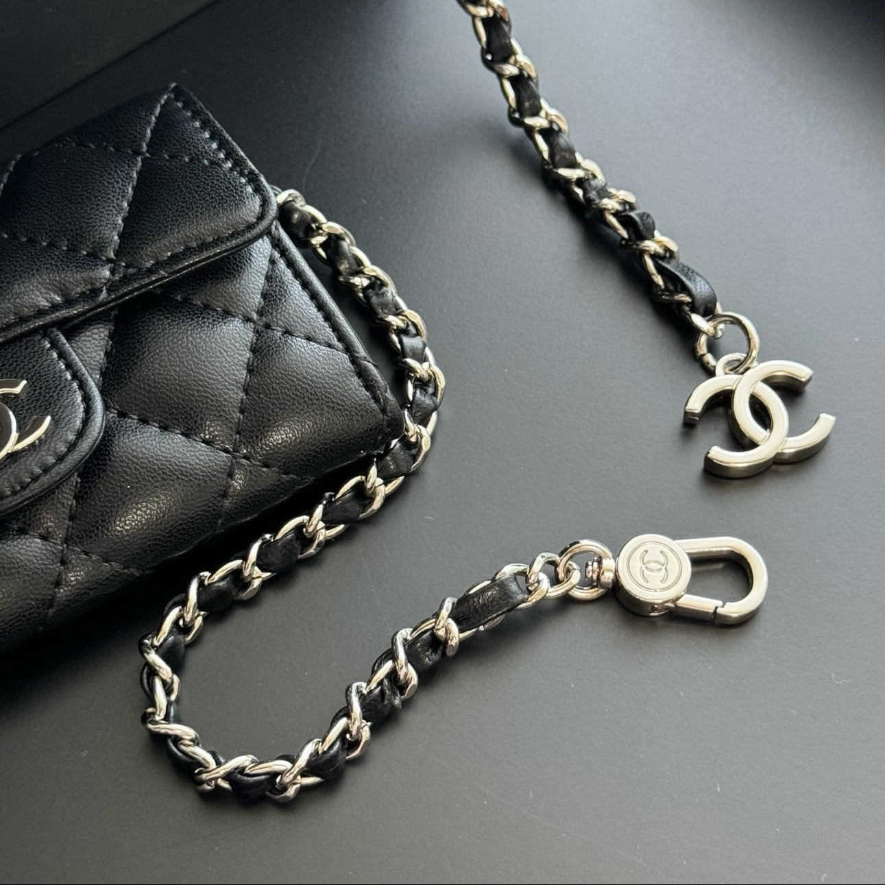Black quilted handbag with a braided chain strap on a dark surface