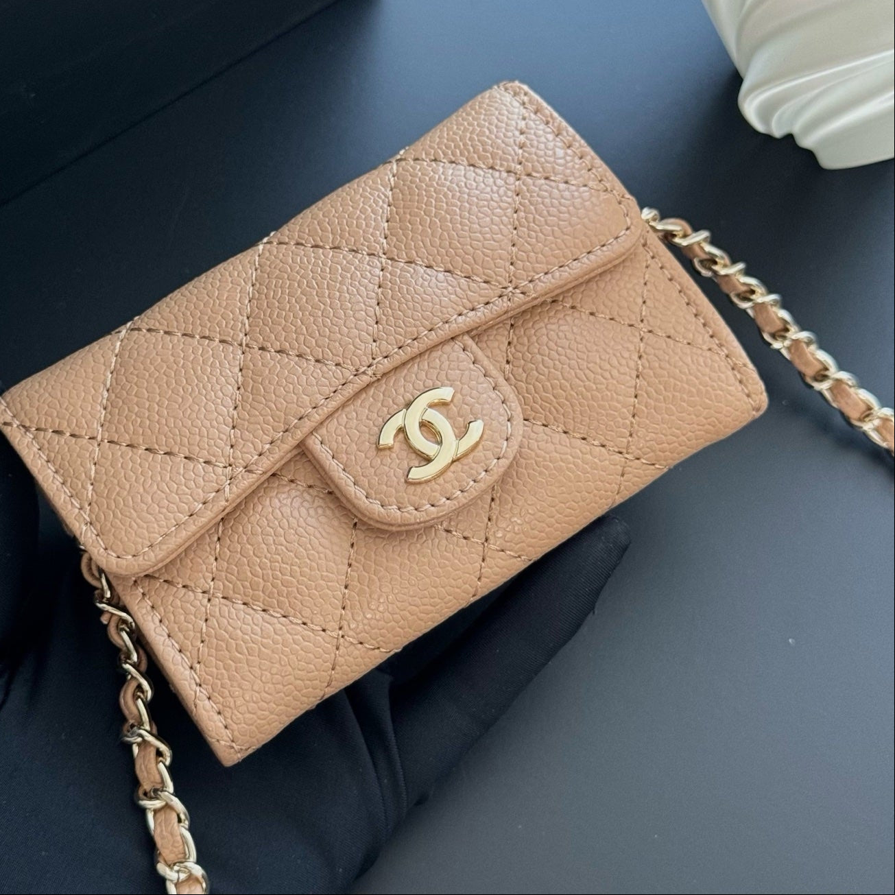 Beige quilted handbag with gold chain on a dark background