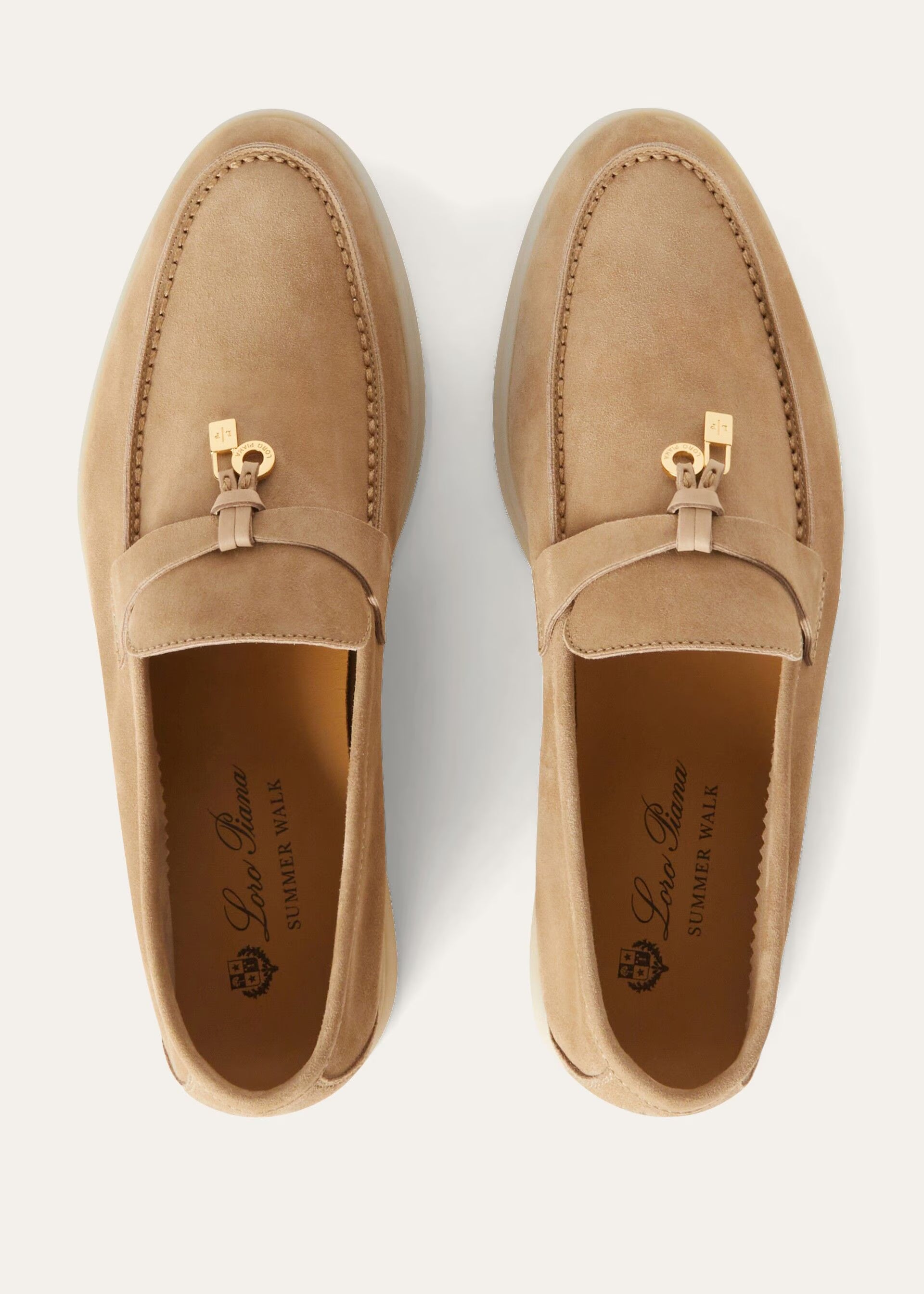 Pair of tan loafers with gold accents on a white background