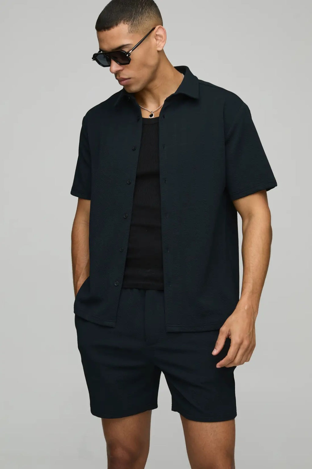 Man wearing a black outfit with sunglasses on a gray background