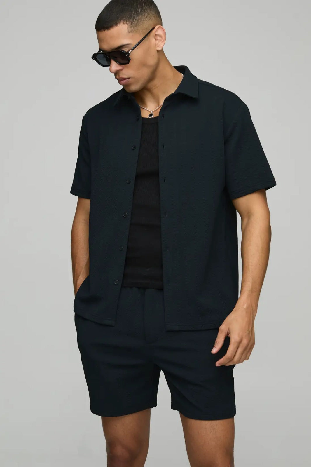 Man wearing a black outfit with sunglasses on a gray background