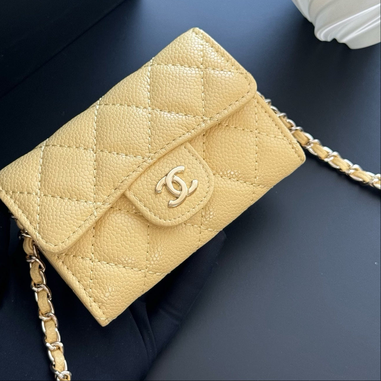 Beige quilted handbag with gold chain on a dark surface