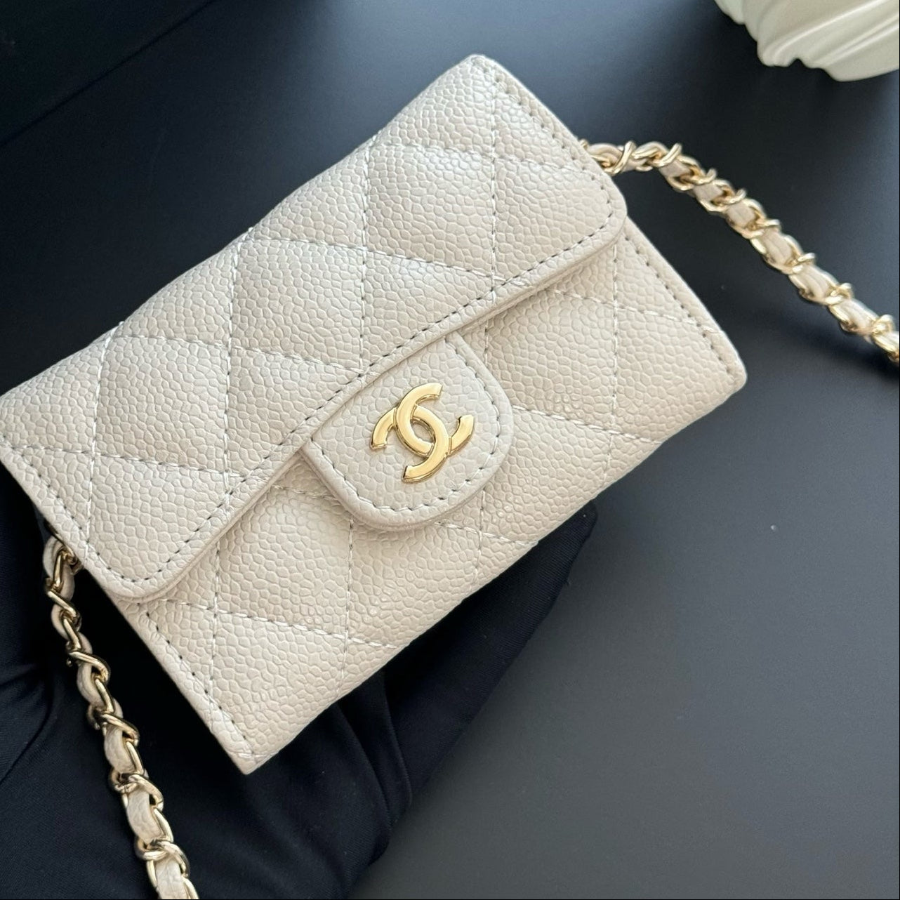 White quilted handbag with gold chain and logo on a dark surface