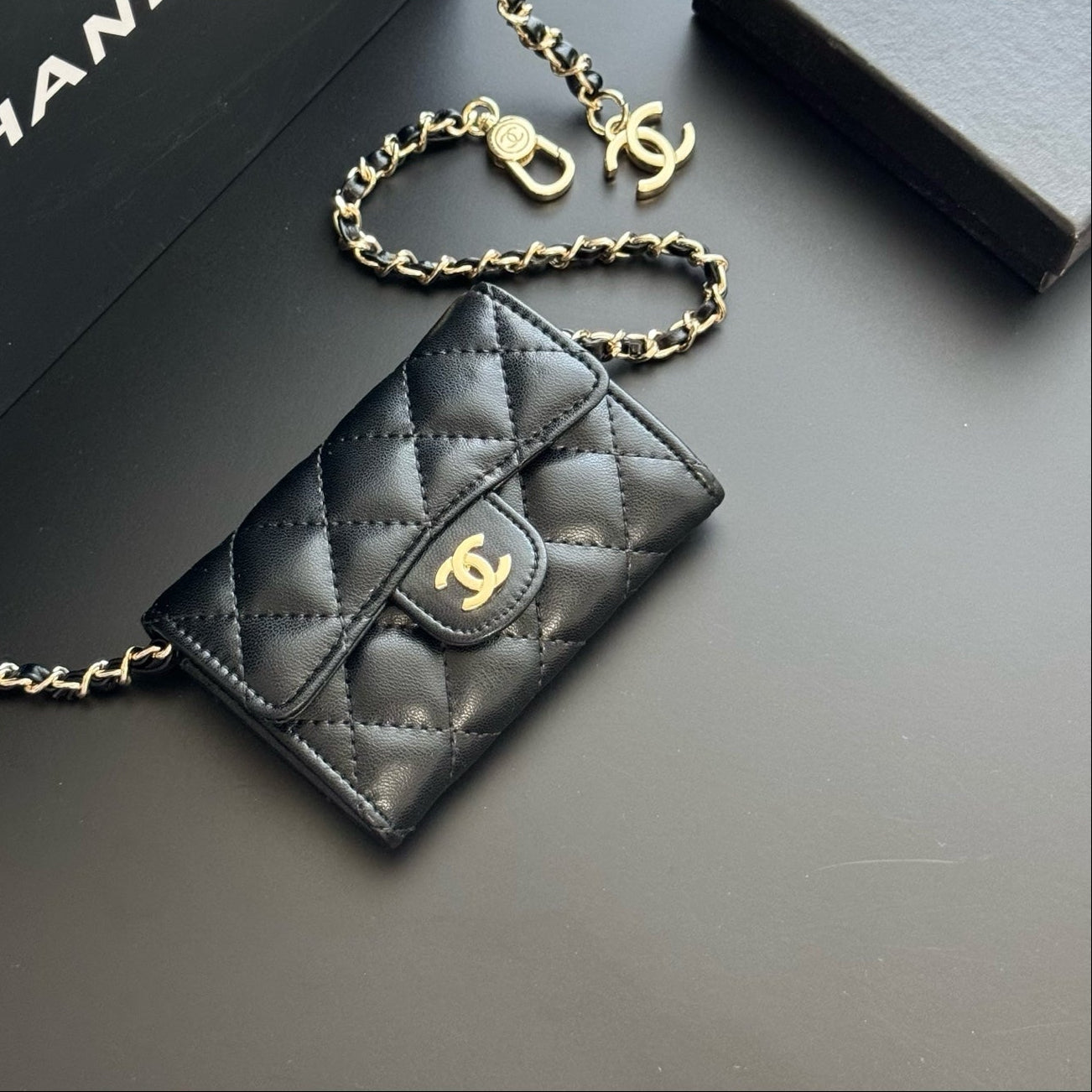Black quilted Chanel wallet with gold chain on a dark surface