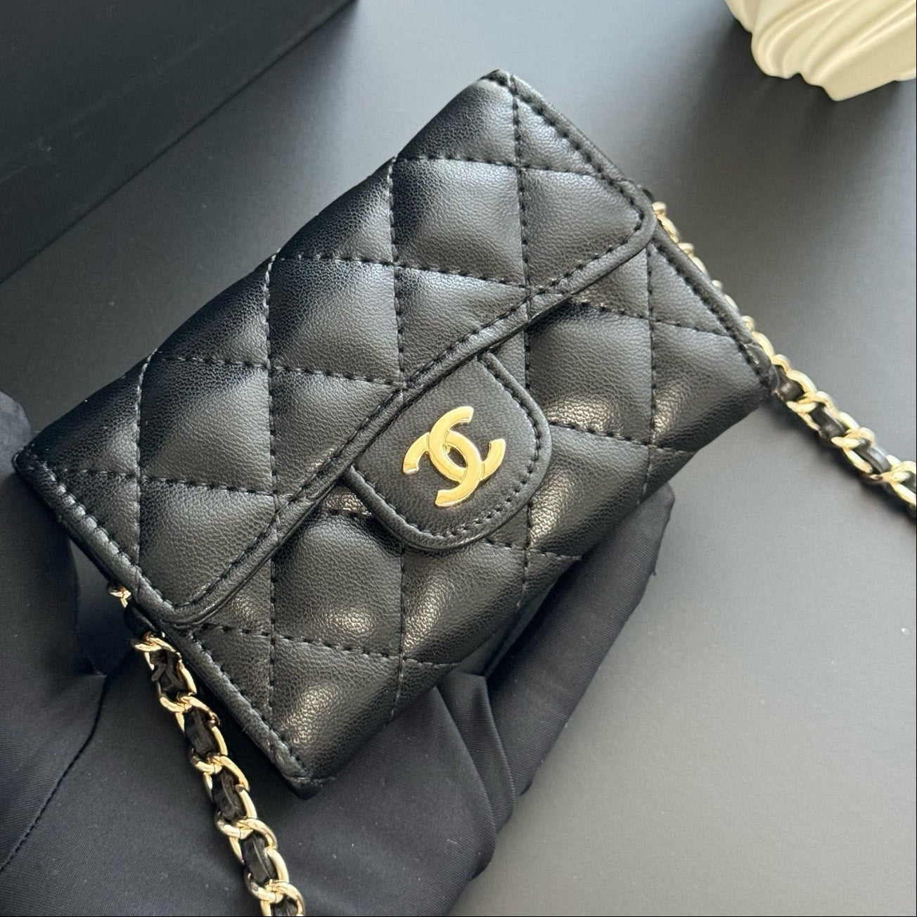 Black quilted handbag with gold chain and logo on a gray surface