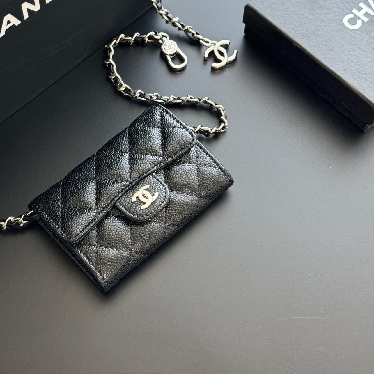 Black quilted Chanel wallet on chain with gold chain and clasp on a dark background.
