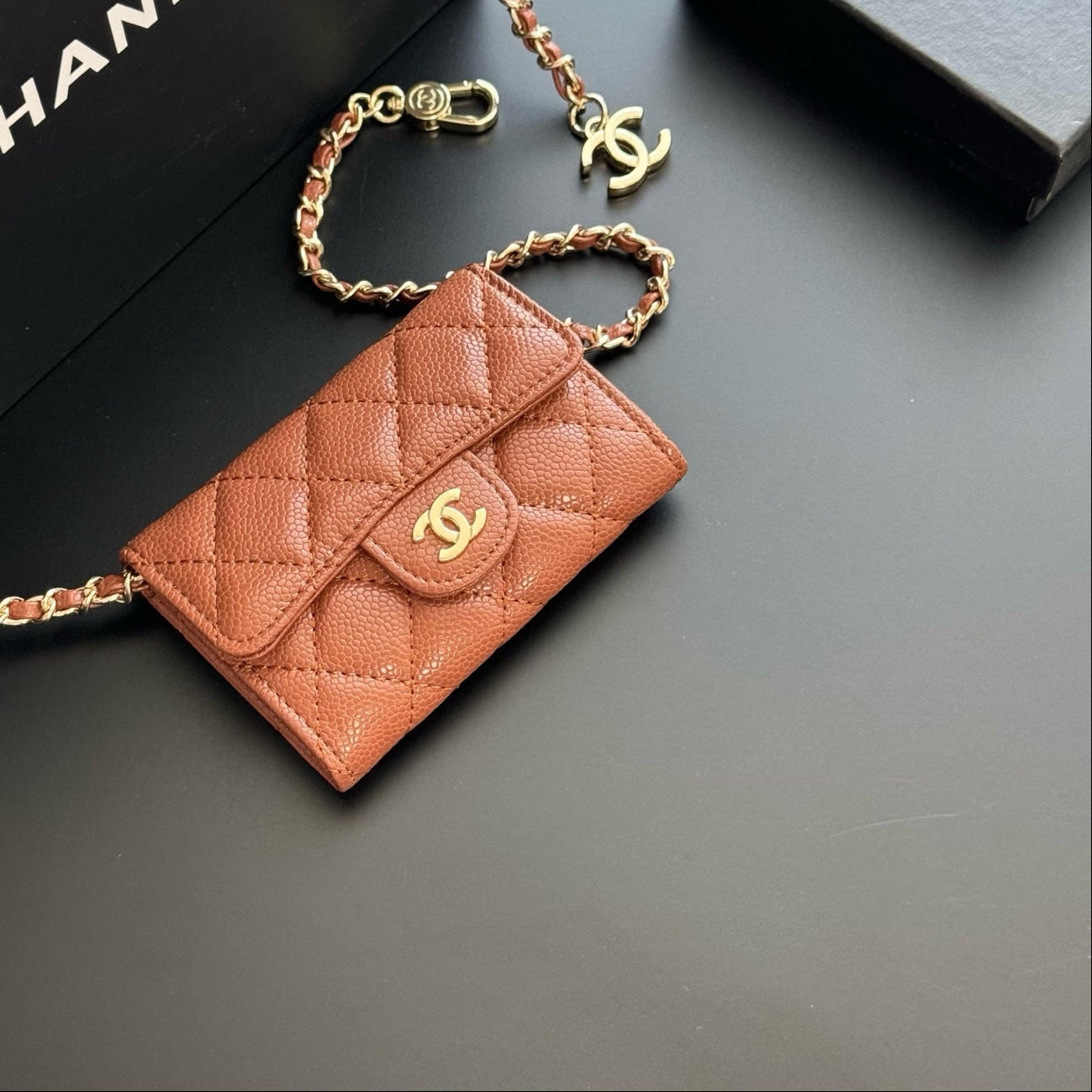 Brown quilted wallet with gold chain on a dark surface with Chanel branding.