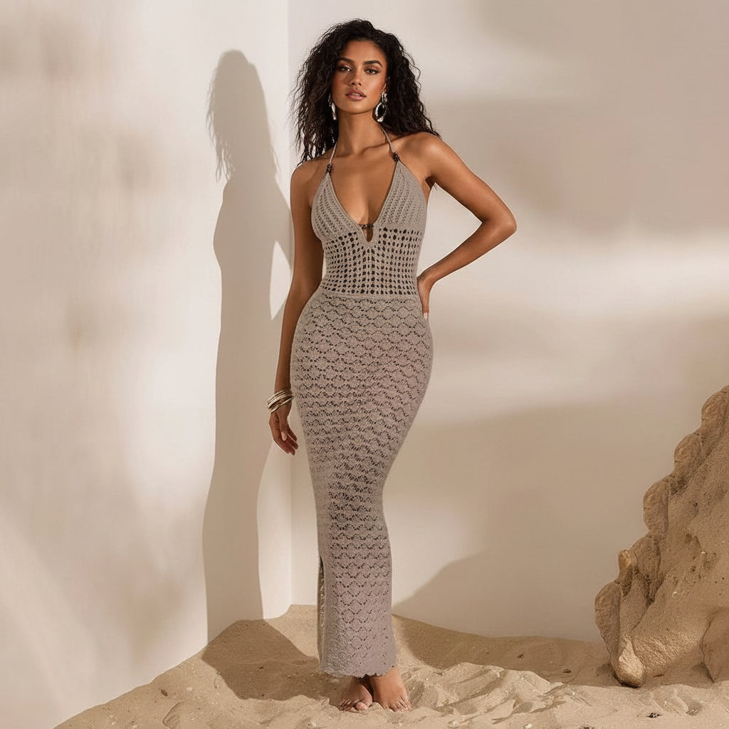 Woman wearing a gray crochet dress standing on sand with a neutral background