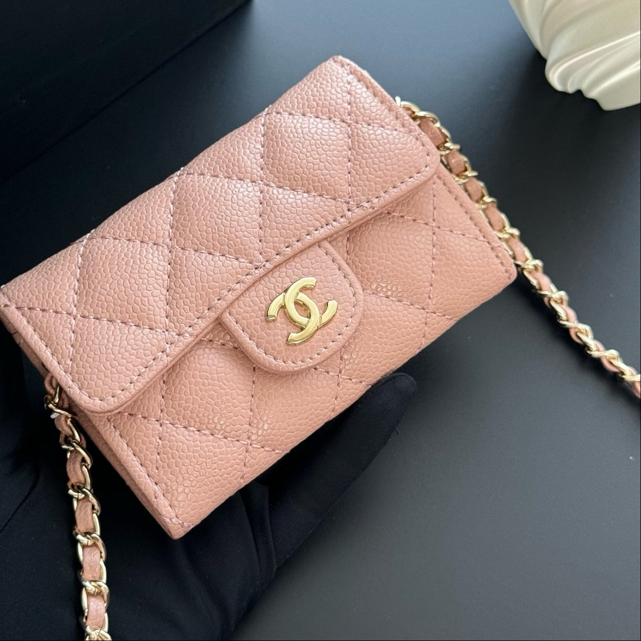 Pink quilted handbag with gold chain and clasp on a dark surface