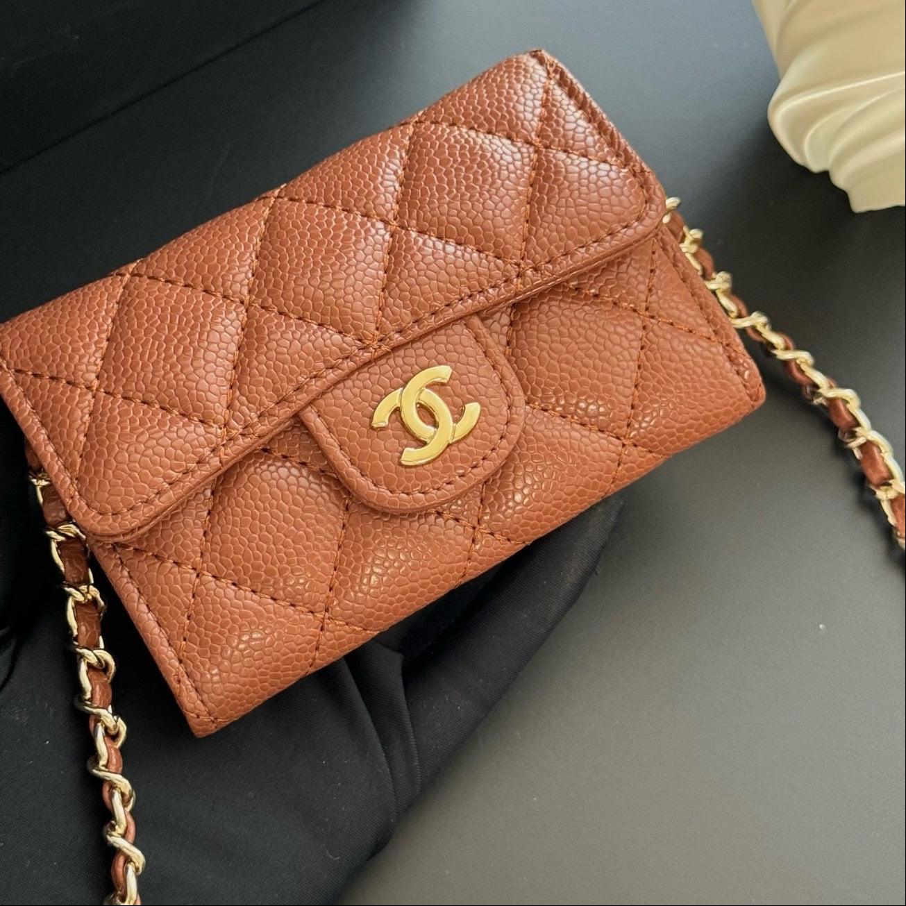 Brown quilted handbag with gold chain on a dark surface