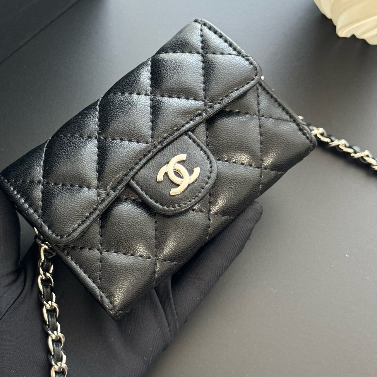 Black quilted handbag with gold chain and logo on a dark surface