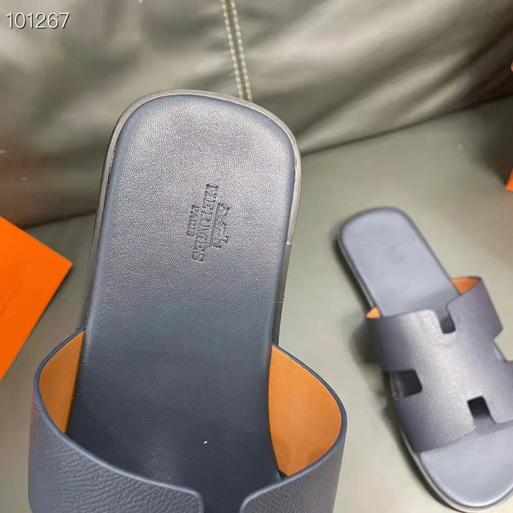 Dar blue sandals with orange interior on a gray surface, featuring a brand logo.